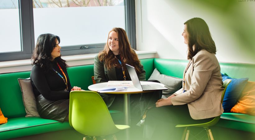Three women who work at PSS are sat at table together. They are smiling and laughing.