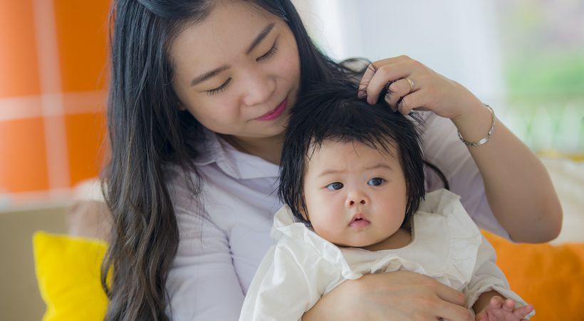 This image shows an Asian woman cuddling her baby, who is wearing a cream baby grow