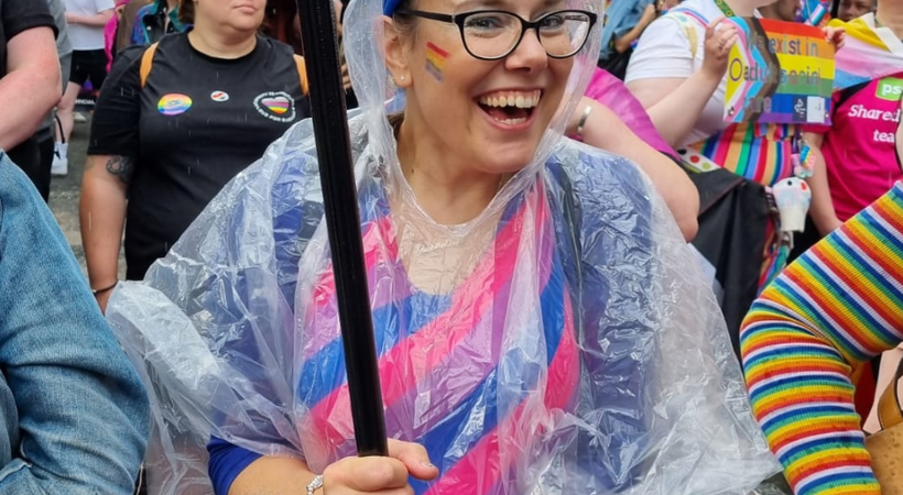 PSS teammate at the Liverpool Pride march, they've got a purple and pink rainbow on their cheek. They are smiling holding an umbrella.